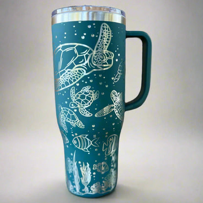 Teal travel mug with white sea turtle and fish design on a light gray background