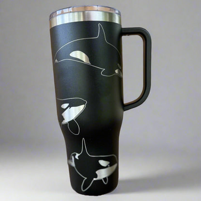 A stainless steel tumbler with a handle, featuring laser engraved Orca whales on a black background